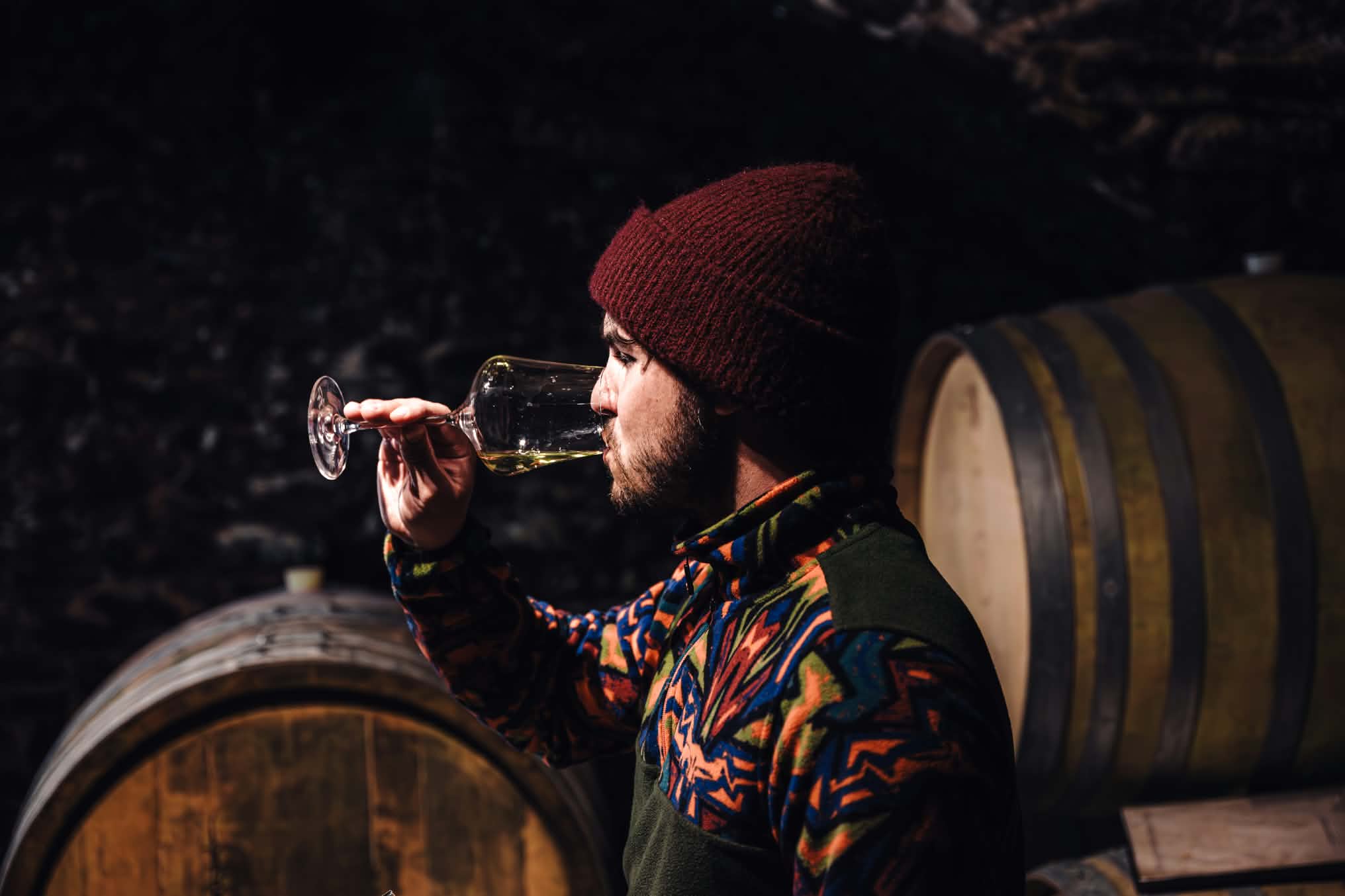 Johannes from Weingut Nehrer tasting white wine among oak barrels in the cellar