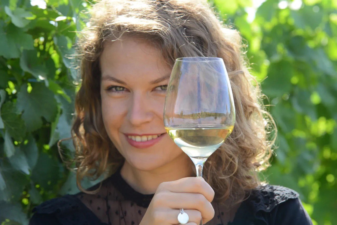 Margot from Domaine Saint-Rémy holding a glass of white wine in front of green vines