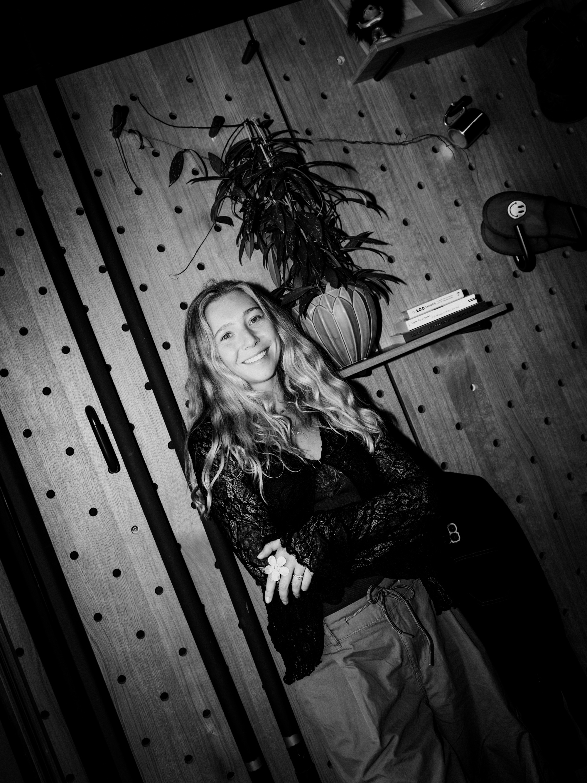 Woman sits against wall with hanging plant overhead.