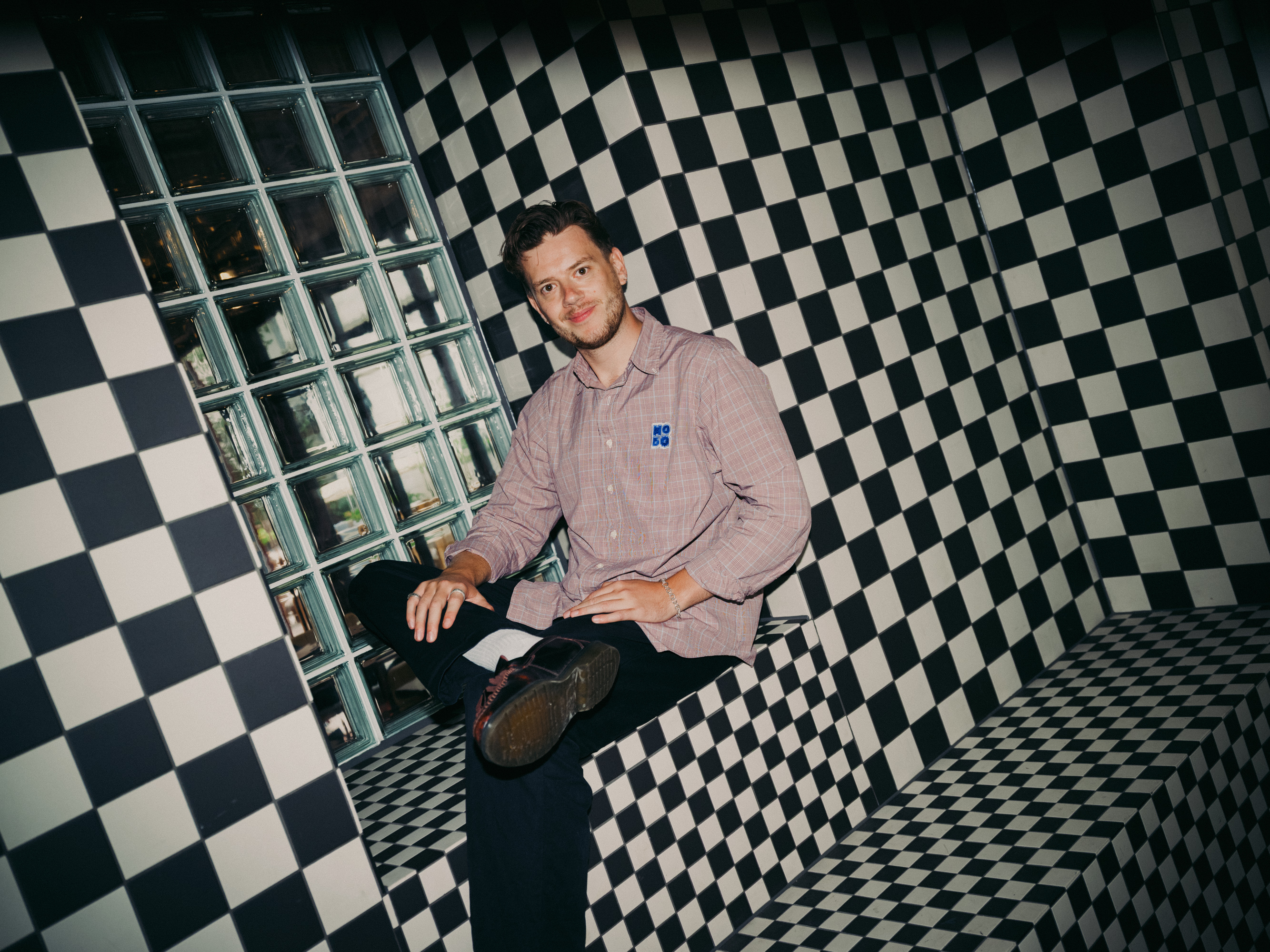 Man sitting on a black and white checkered bench next to a glass block wall