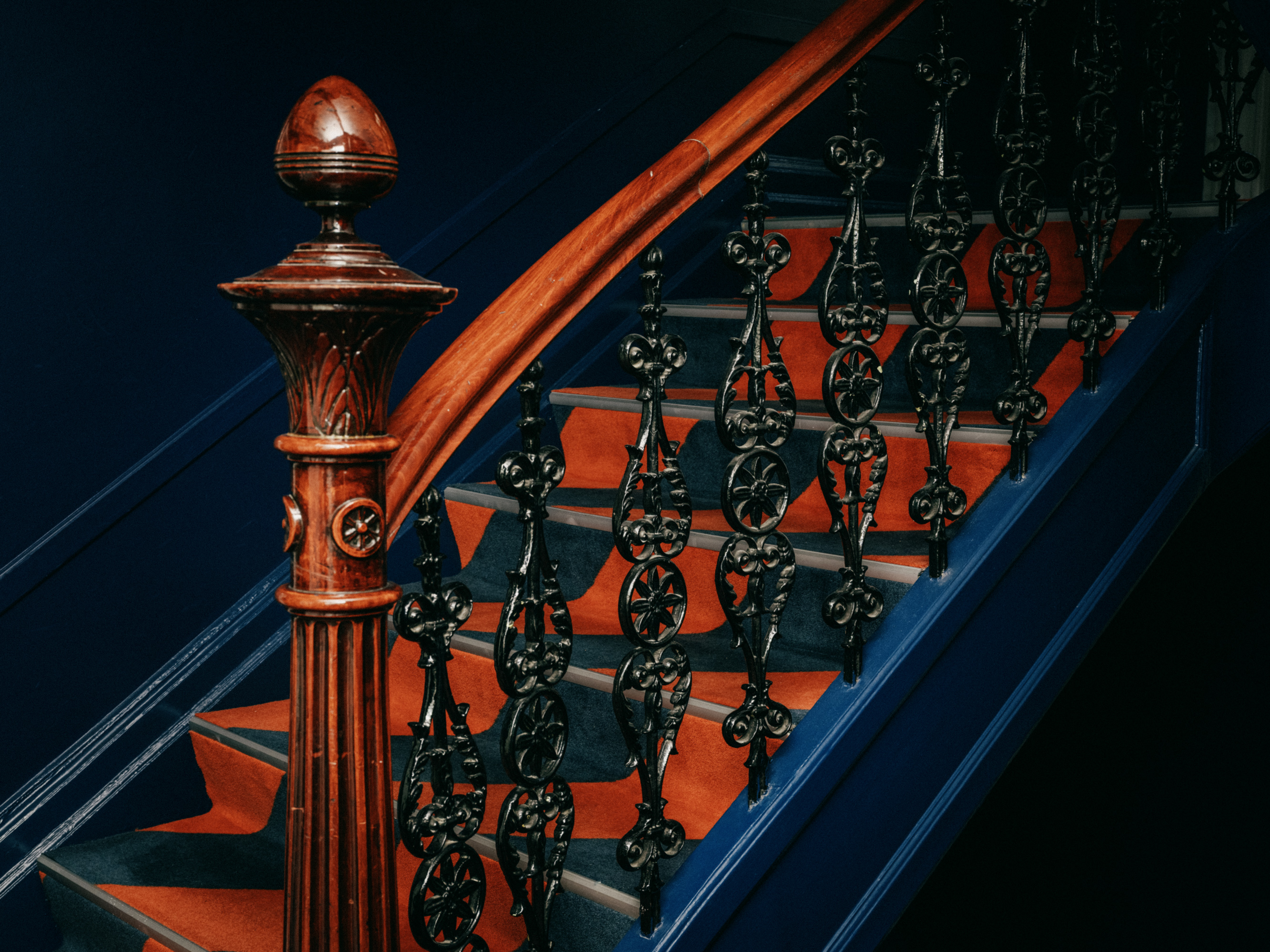 Carved wooden newel post and wrought iron railing on an orange and blue staircase