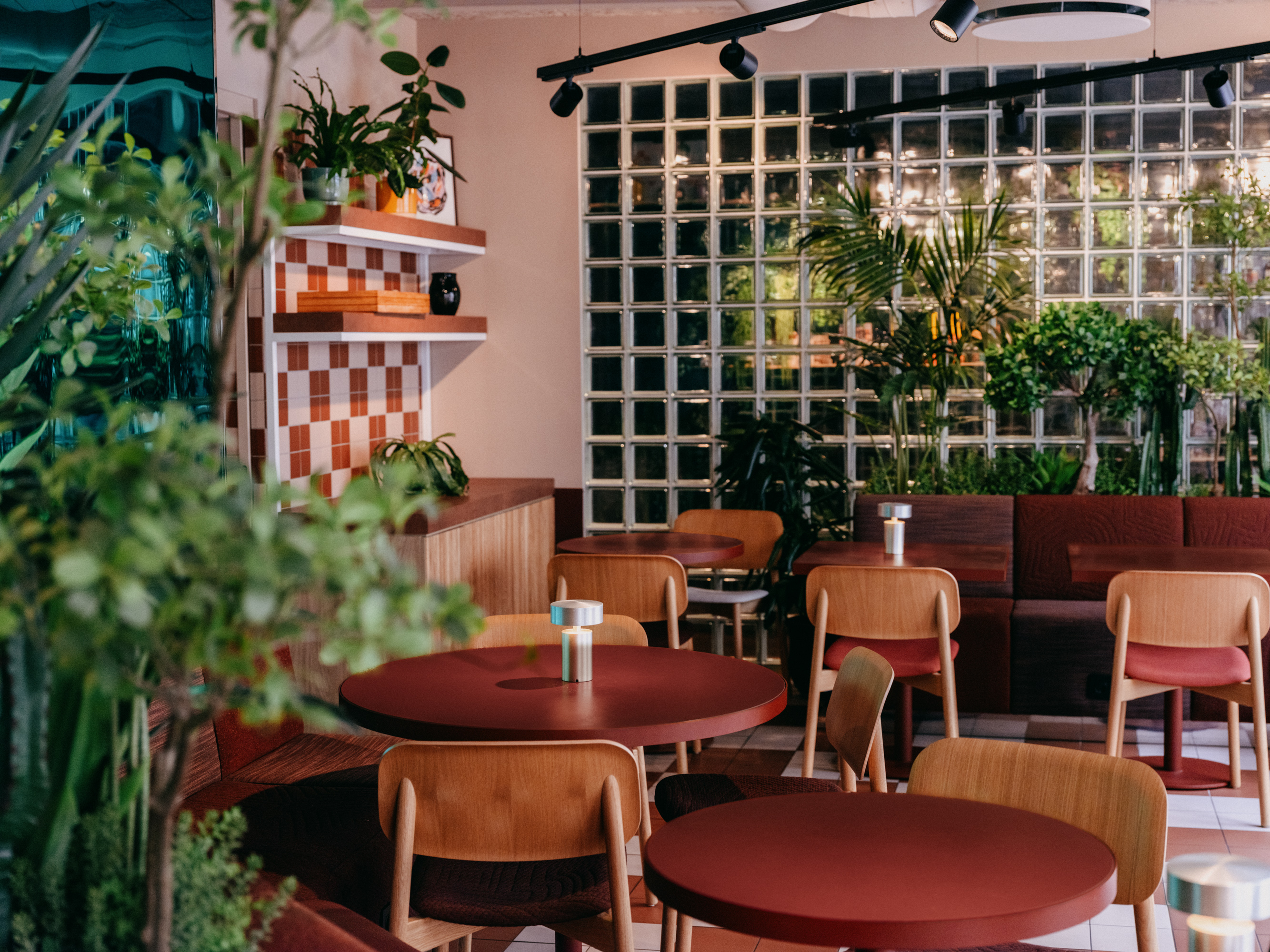 Bright restaurant with red tables, wooden chairs and lots of plants