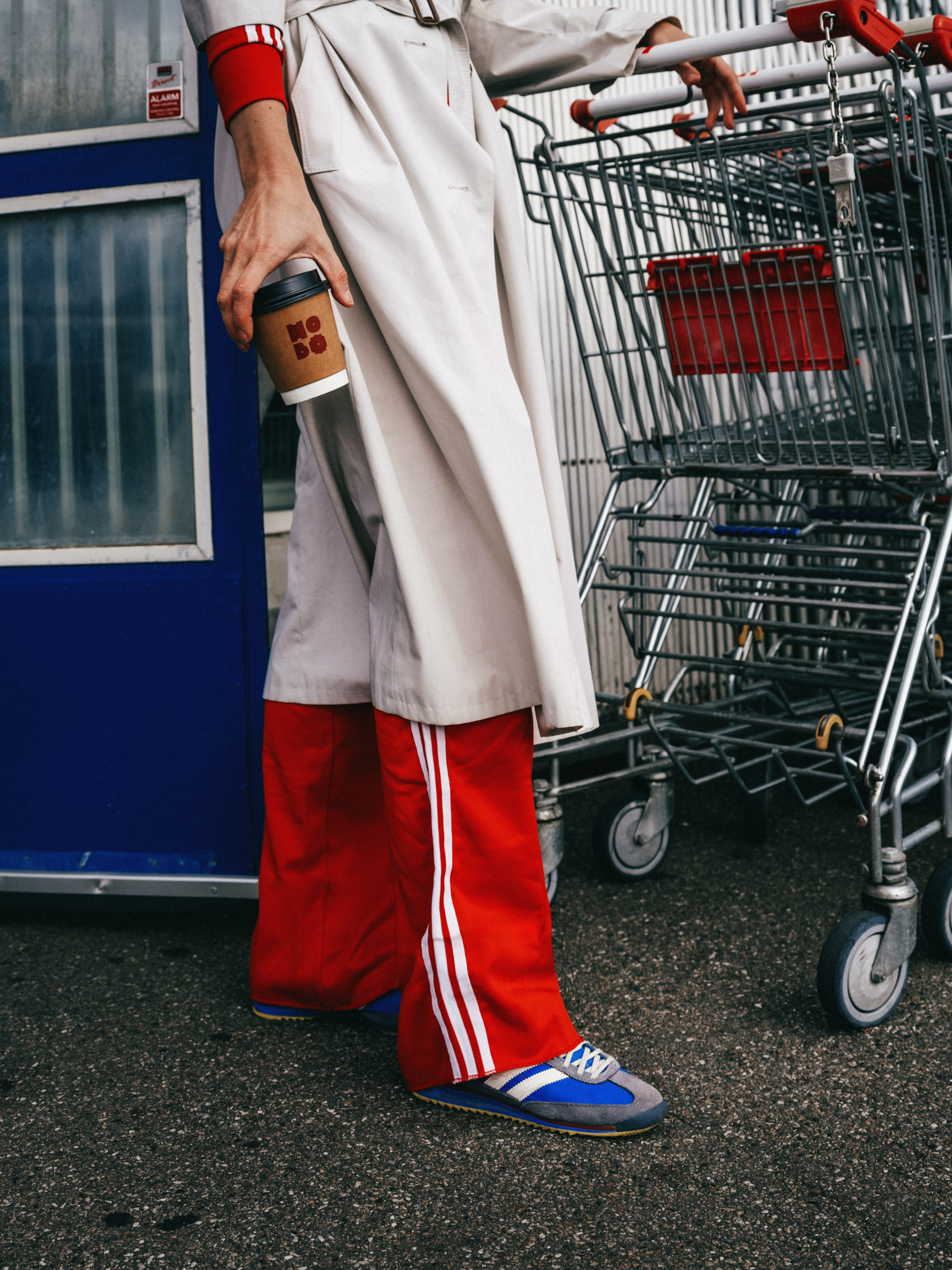 Person in red track pants holding a Hobo coffee cup next to shopping carts