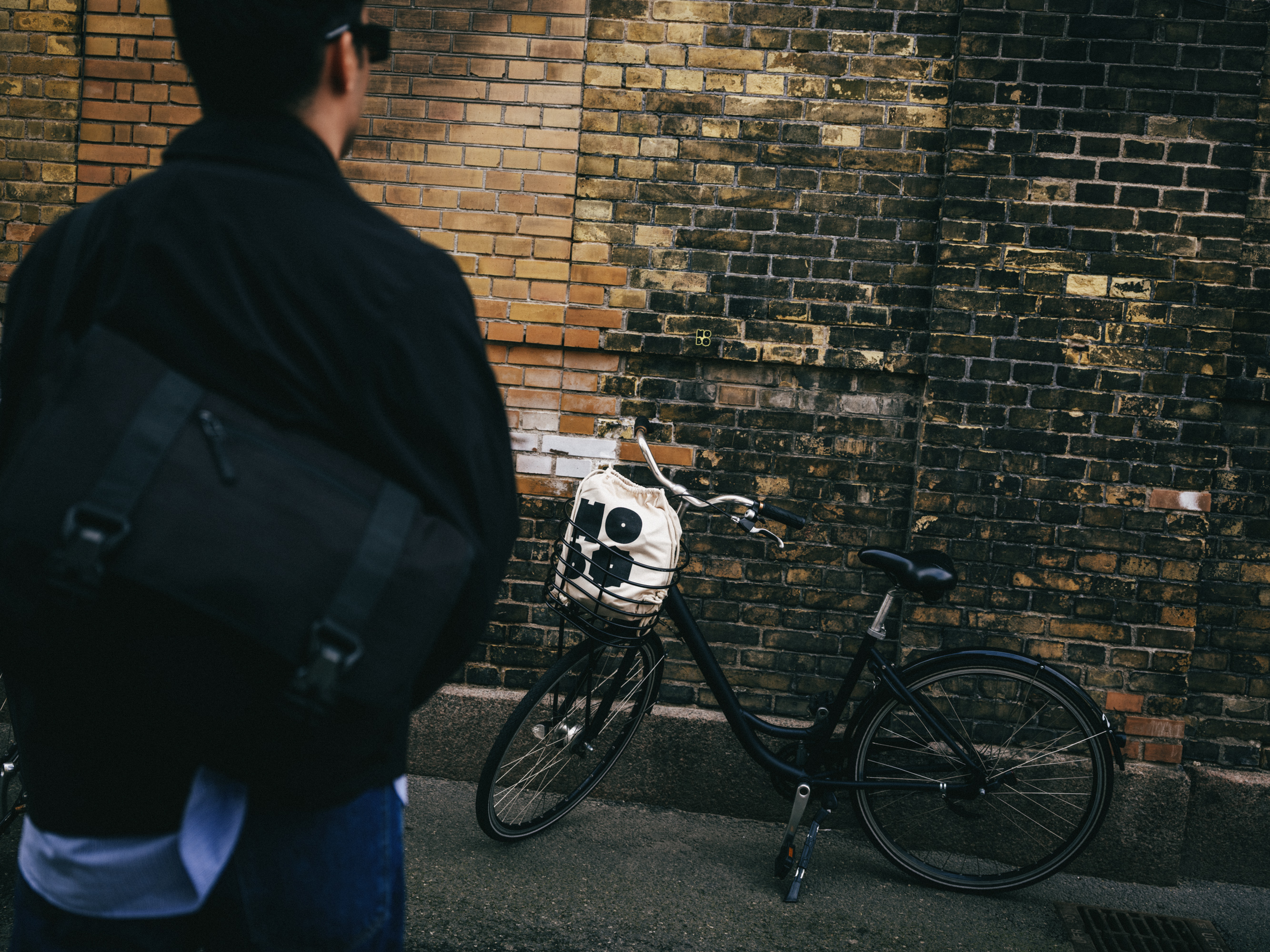 Person with a backpack by a bicycle against a brick wall