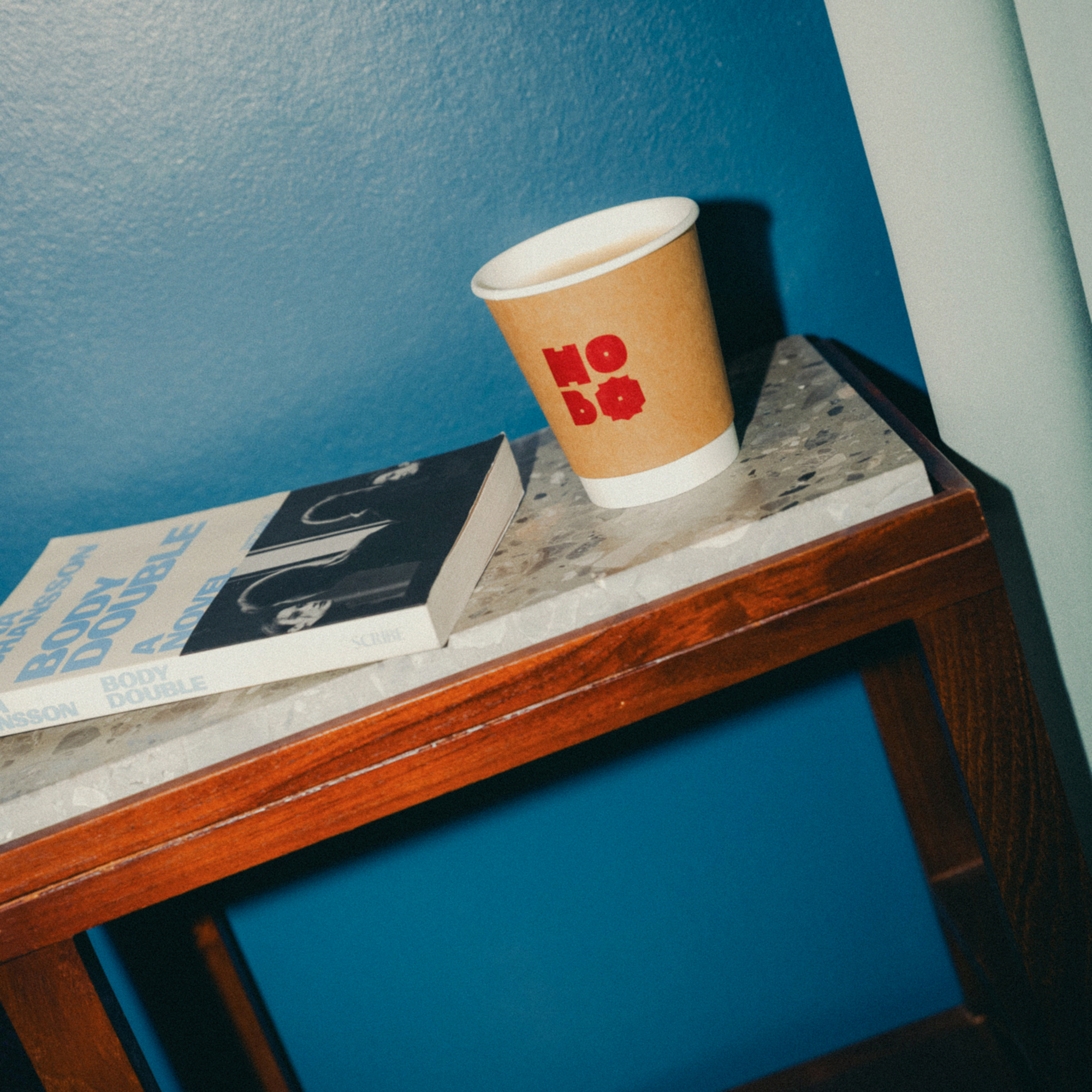 Hobo coffee cup and a book on a bedside table against a blue wall