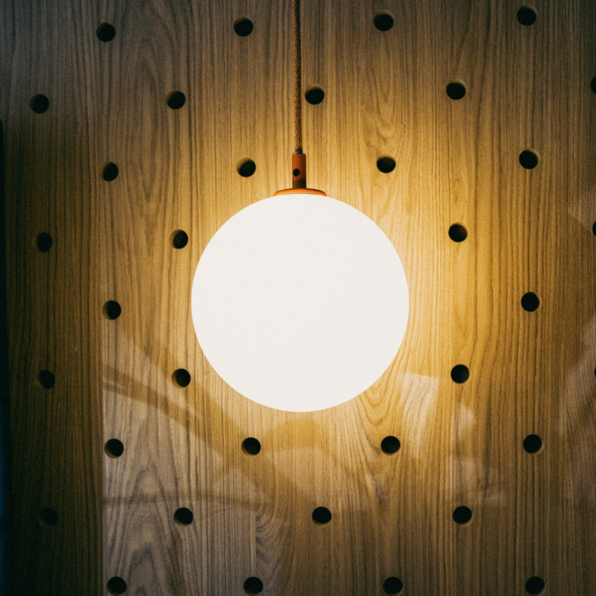 Round pendant lamp glowing against a wooden peg wall