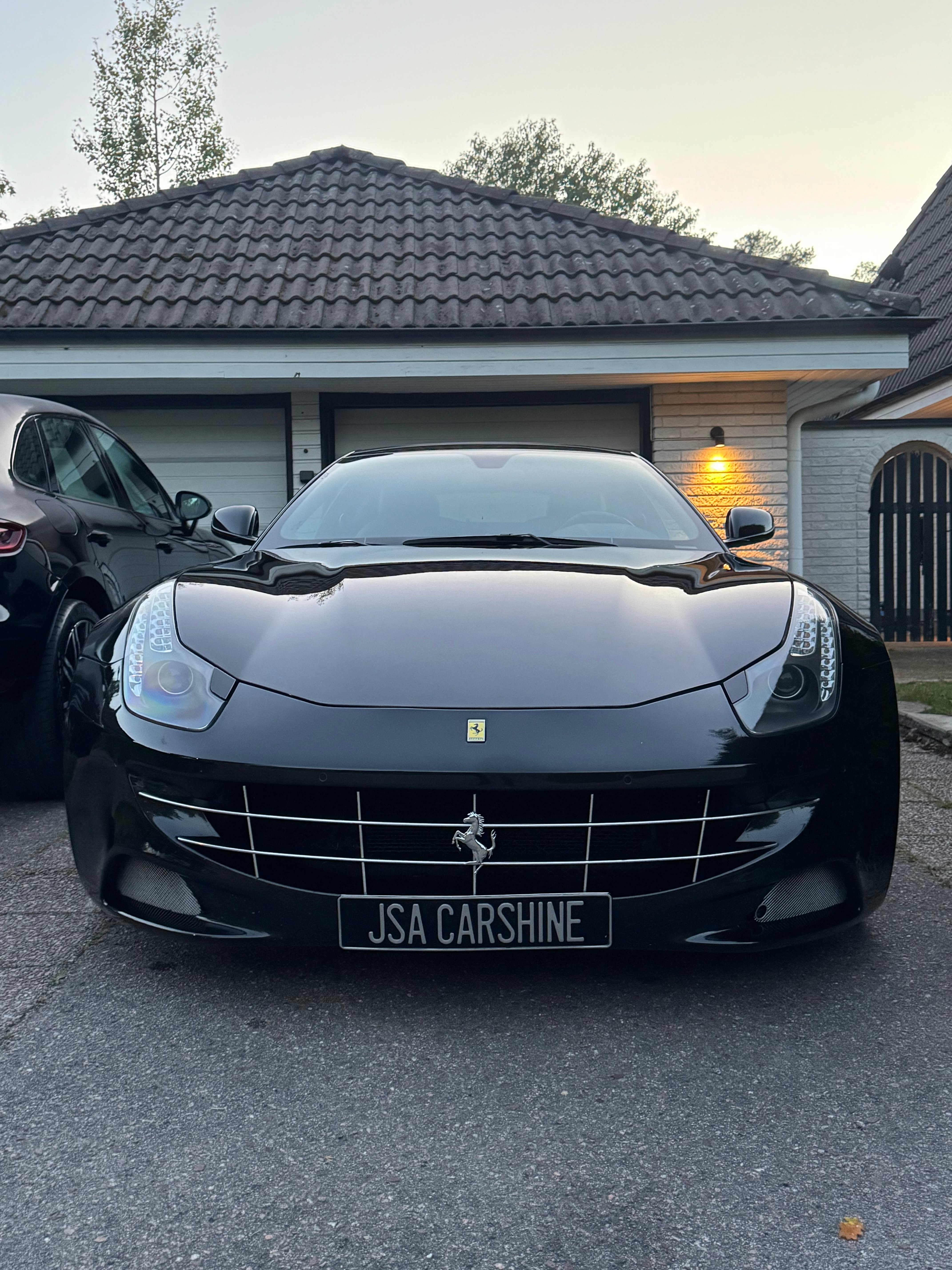 Svart Ferrari FF med JSA Carshine-skylt framför garage i skymning