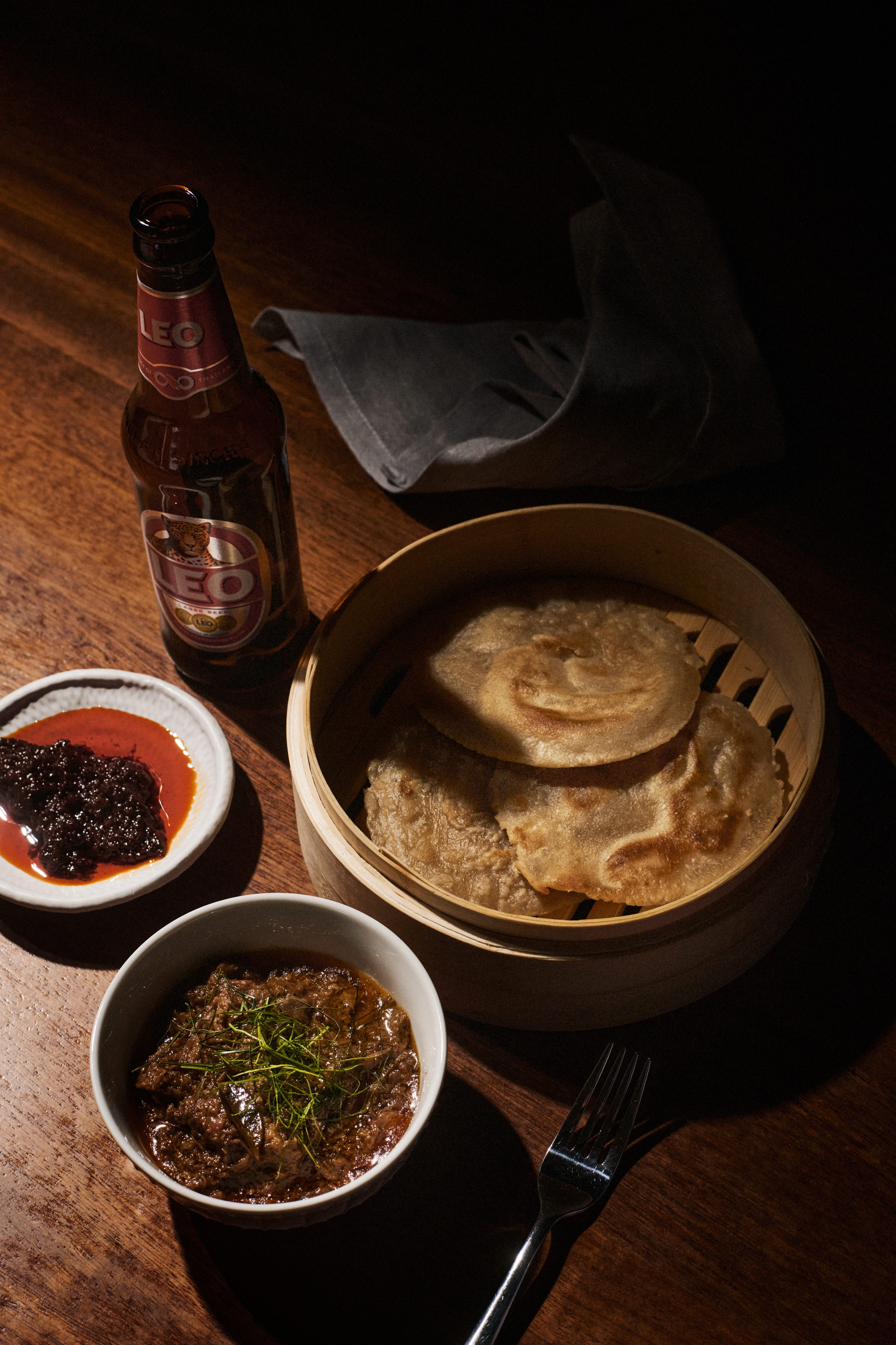 Roti in bamboo basket with curry, chili sauce, and a bottle of Leo beer