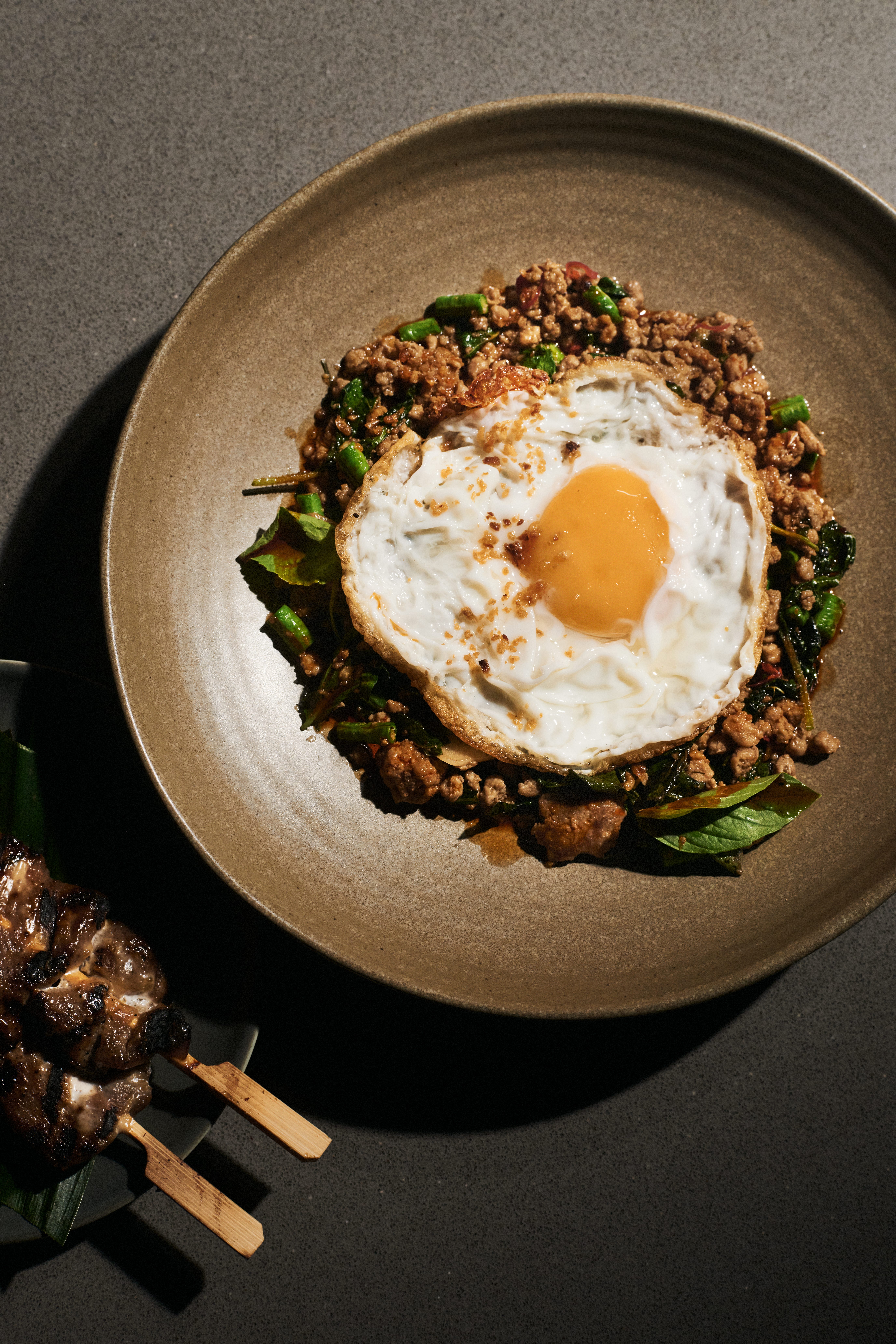 Wokad färs med thaibasilika och stekt ägg, bredvid grillspett